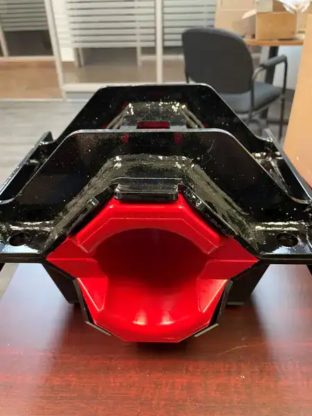 A black and red industrial mount or bracket sits on a wooden desk; office chairs and glass partitions are visible in the background.