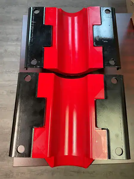 Two large industrial pipe saddles with red curved centers and black flat edges, placed side by side on a table. Four bolt holes are visible on each saddle, two on each side.