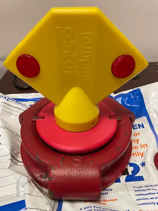 A yellow and red plastic lock device is attached to a red industrial valve, placed on top of a white and blue plastic bag. The yellow part has a diamond shape with two red circles and the word "tempio" embossed on it.