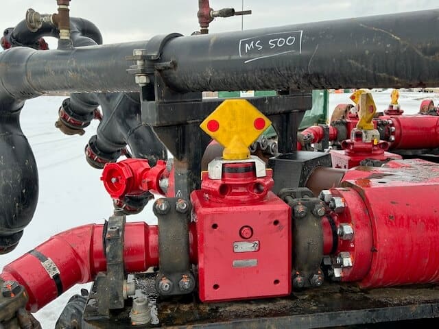 A close-up view of industrial piping and valves, featuring a prominent yellow and red valve handle labeled "MS 500." The equipment is set outdoors, with snow visible in the background.