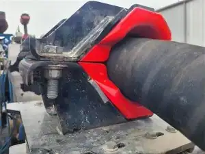 Close-up of a large black cylindrical pipe secured with a red clamp and black metal bracket, fastened by bolts, likely part of industrial machinery or equipment.